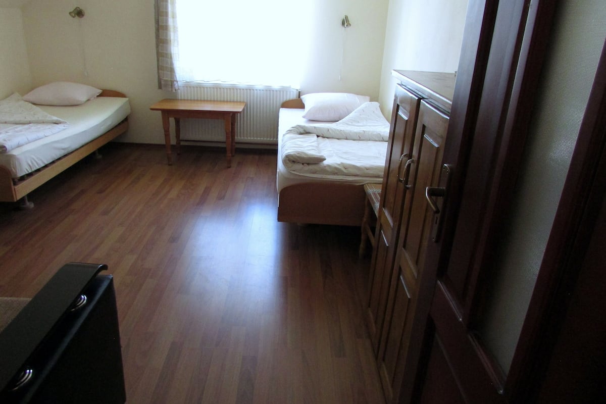 Une petite pièce simple, avec deux lits simples, une table en bois et une armoire.