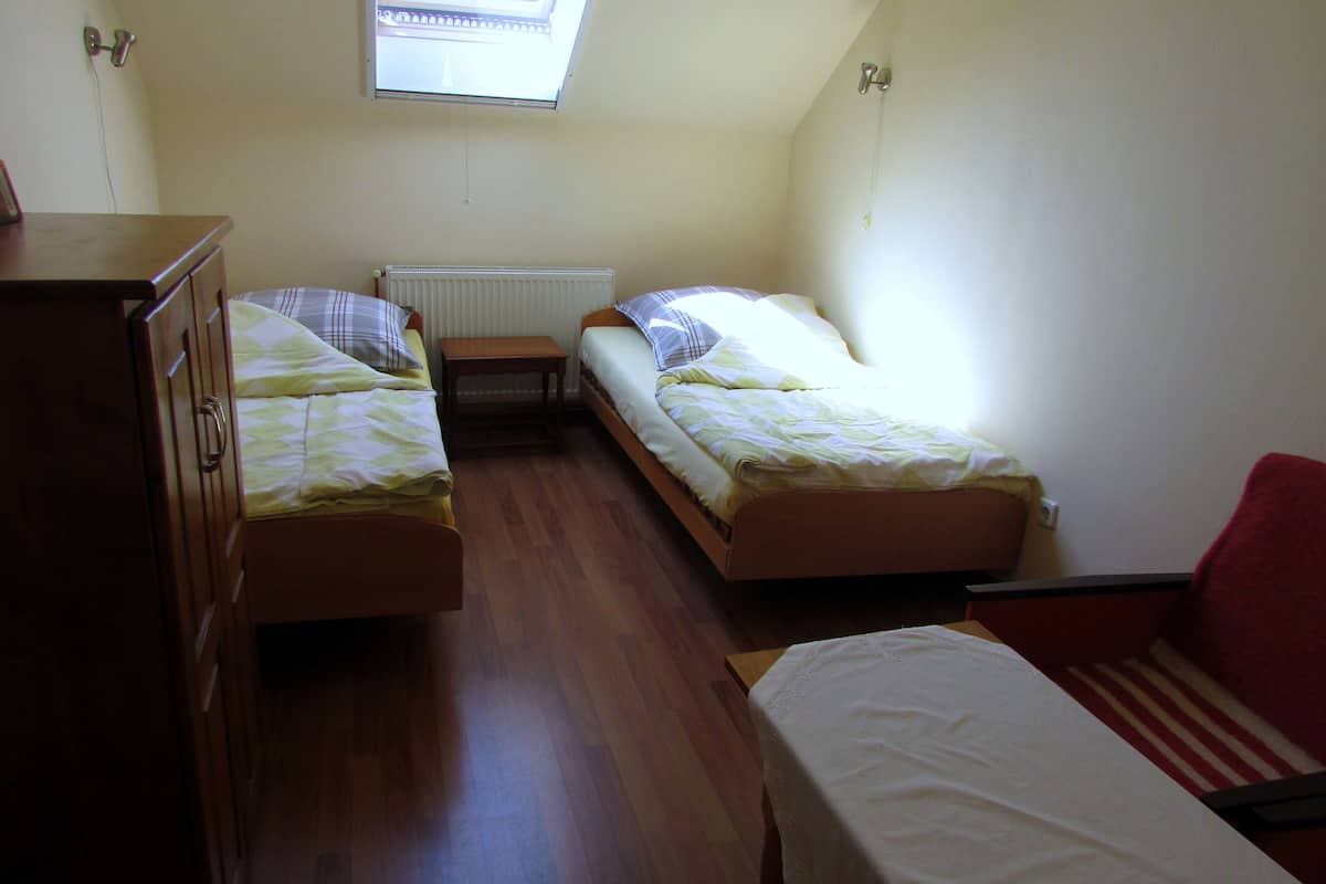 Une petite pièce bien éclairée, avec deux lits simples, une commode en bois et une chaise rouge.
