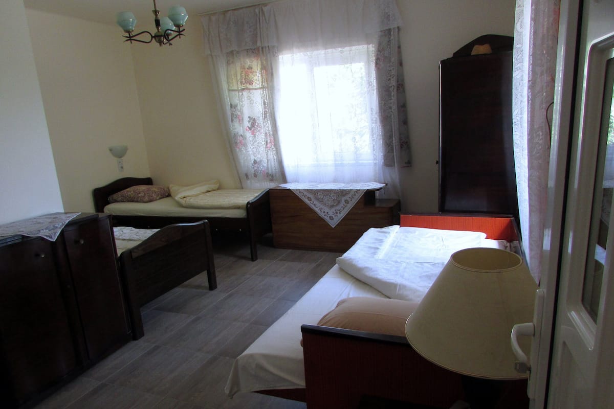Une chambre à coucher avec un lit, une table de chevet, une chaise, une armoire et une fenêtre avec des rideaux.