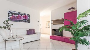 A modern living room with a white sofa, a glass coffee table, a pink entertainment unit, and a large potted plant. - Penthouse (Roseto degli Abruzzi)