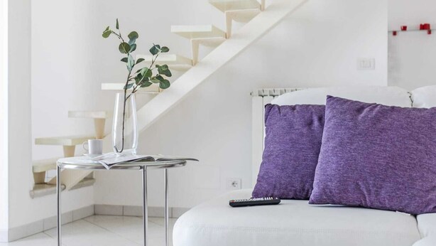 A modern living room with a white sofa, a glass coffee table, a vase with a plant, and a staircase. - Penthouse (Roseto degli Abruzzi)
