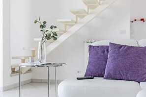 A modern living room with a white sofa, a glass coffee table, a vase with a plant, and a staircase. - Penthouse (Roseto degli Abruzzi)
