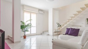 A modern living room with a white sofa, a staircase, and a potted plant. - Penthouse (Roseto degli Abruzzi)
