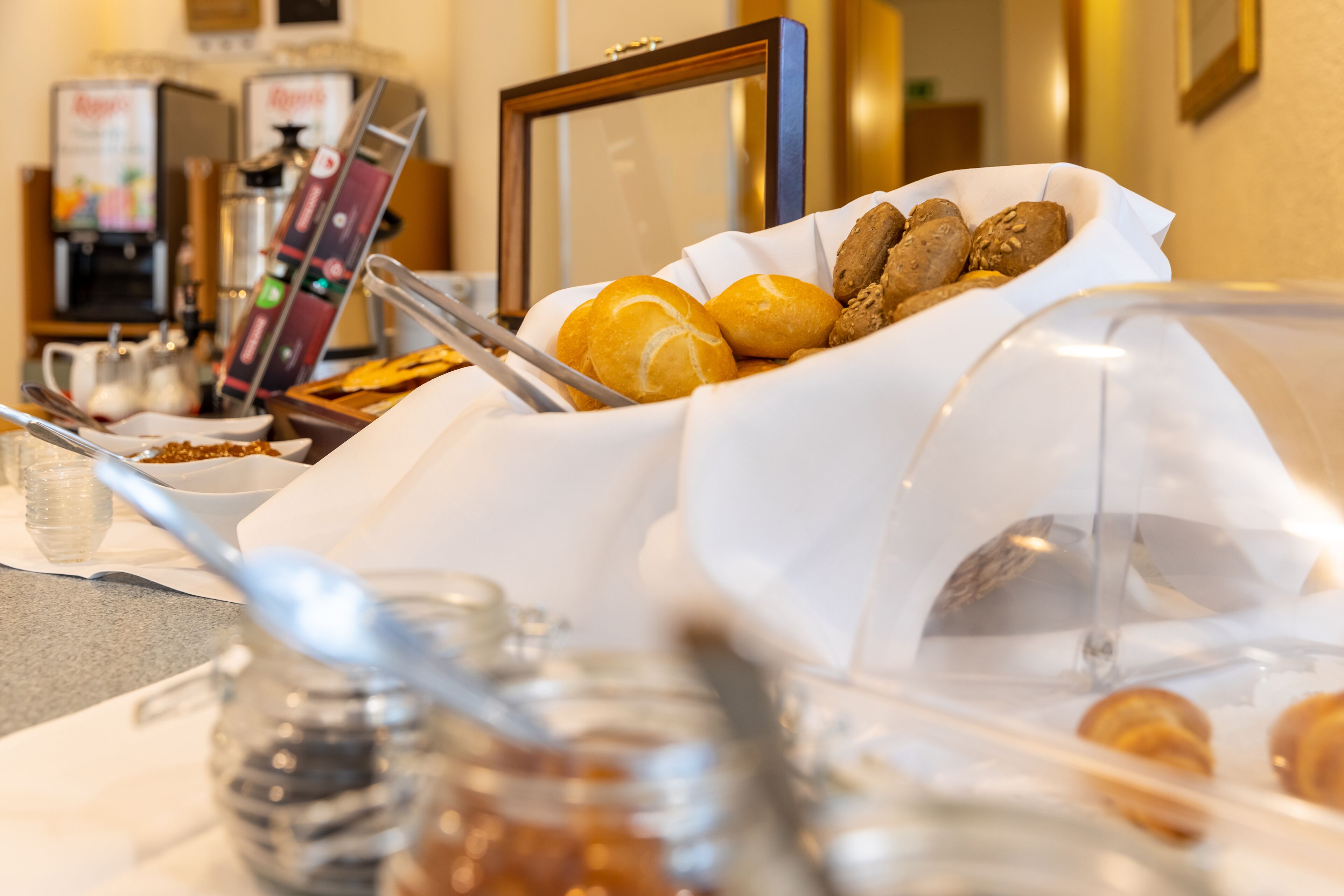 A breakfast buffet with various pastries and bread, a coffee machine, and condiments in the foreground.