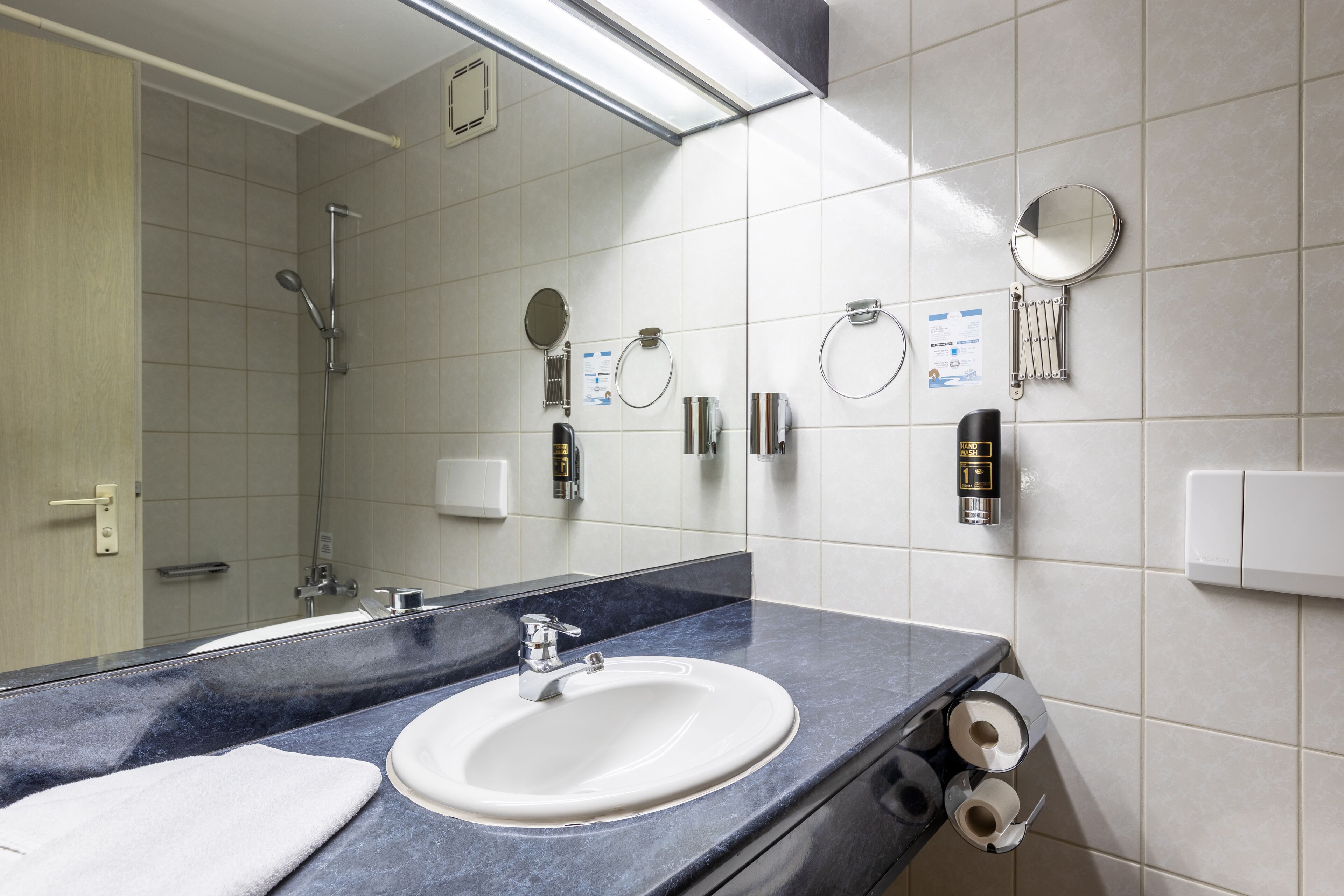 A modern bathroom with a large mirror, a sink, and a shower.