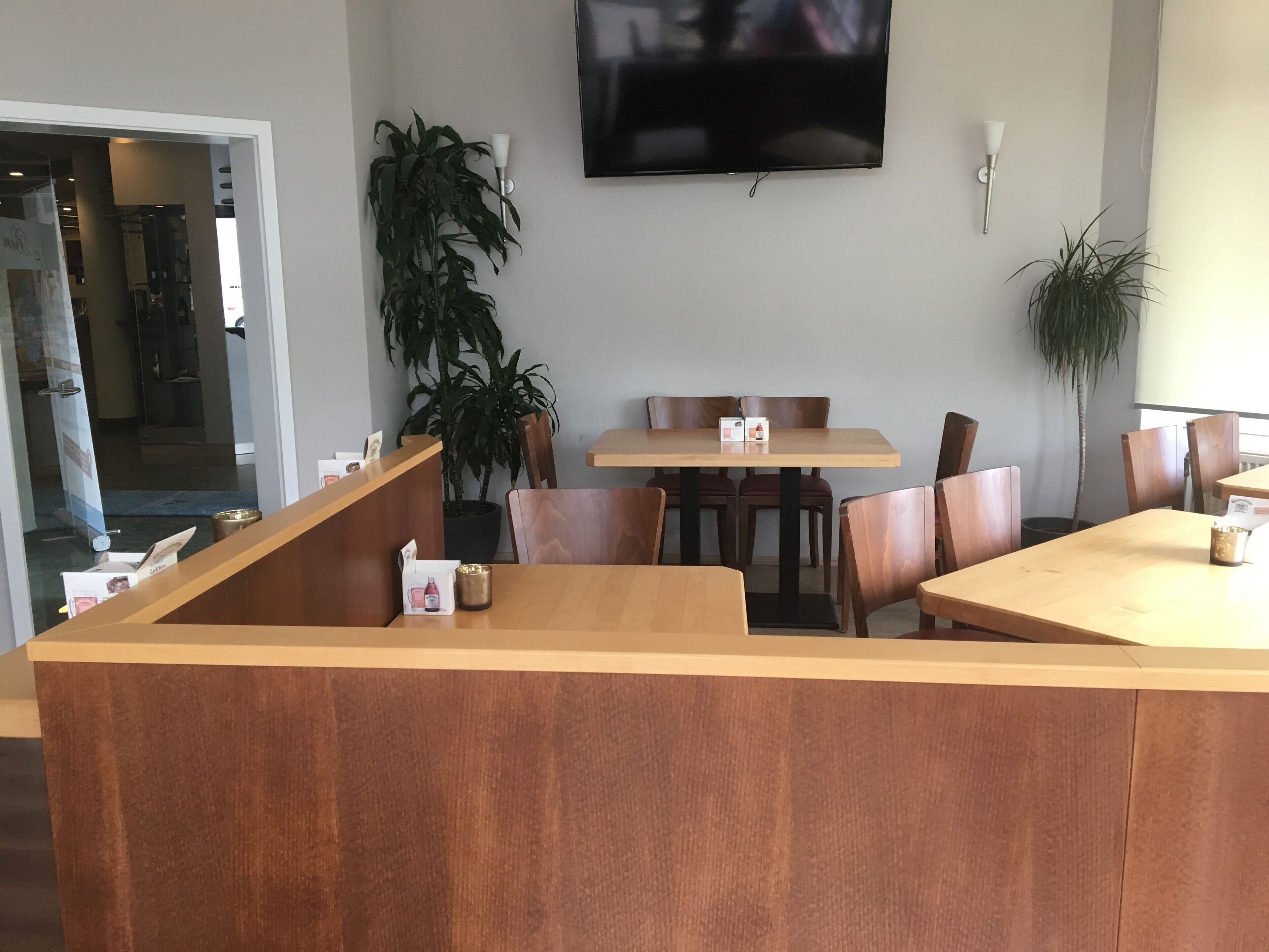 Un restaurant avec des tables et des chaises en bois, un téléviseur fixé au mur et des plantes en pot.