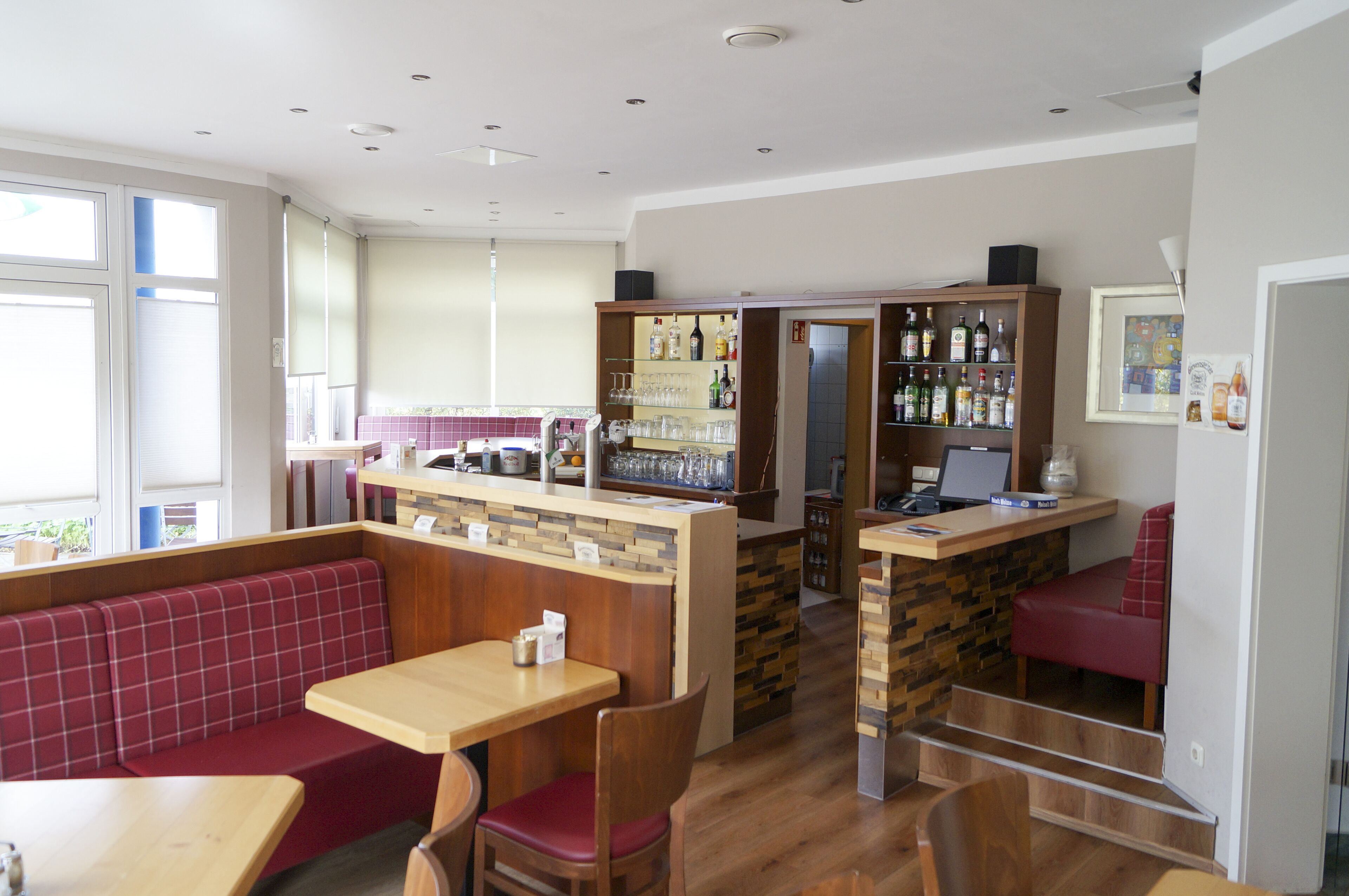 Un restaurante con zona de bar, asientos con cojines rojos y una barra de madera.