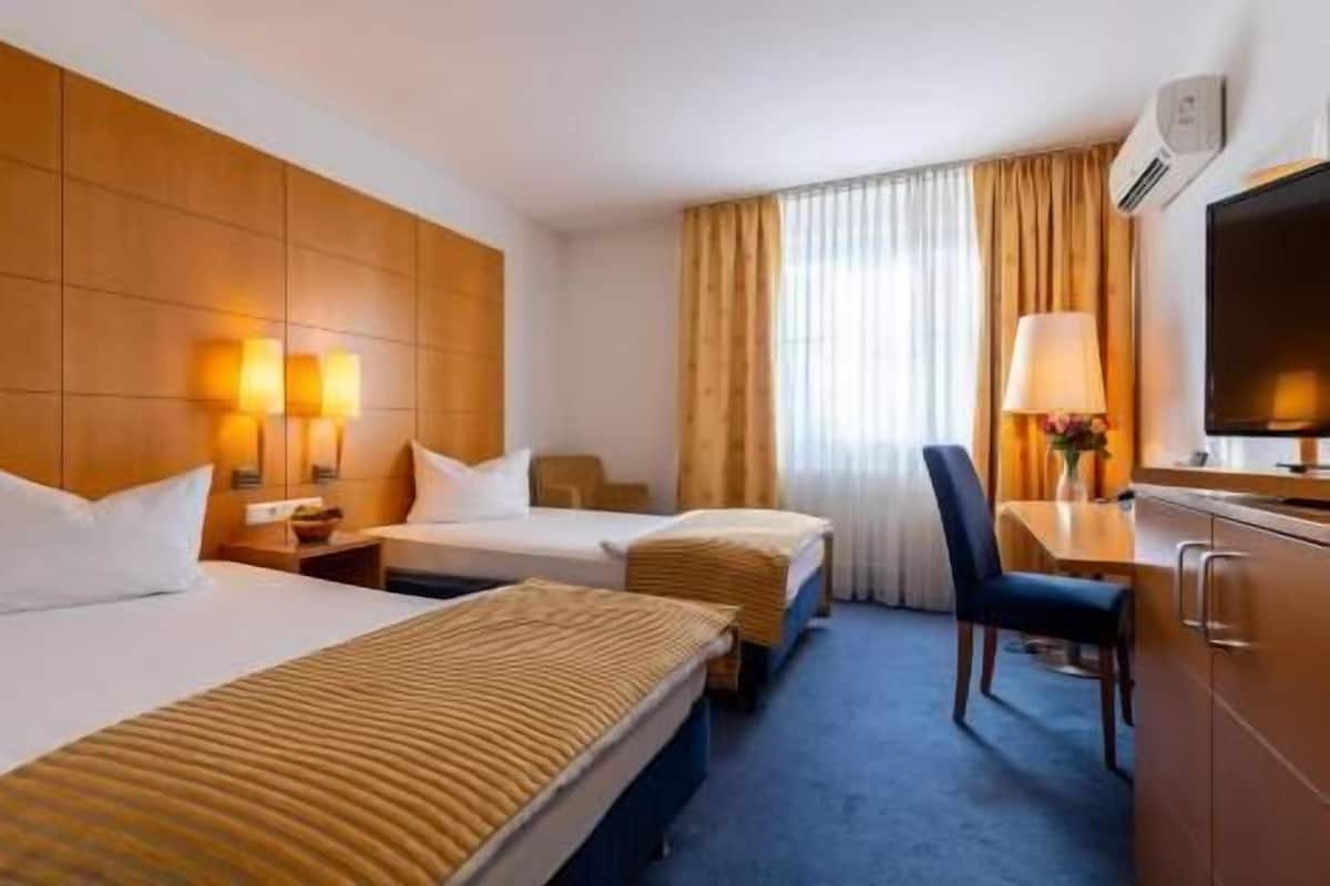 A hotel room with two beds, a desk with a chair, a television, and a window with curtains.
