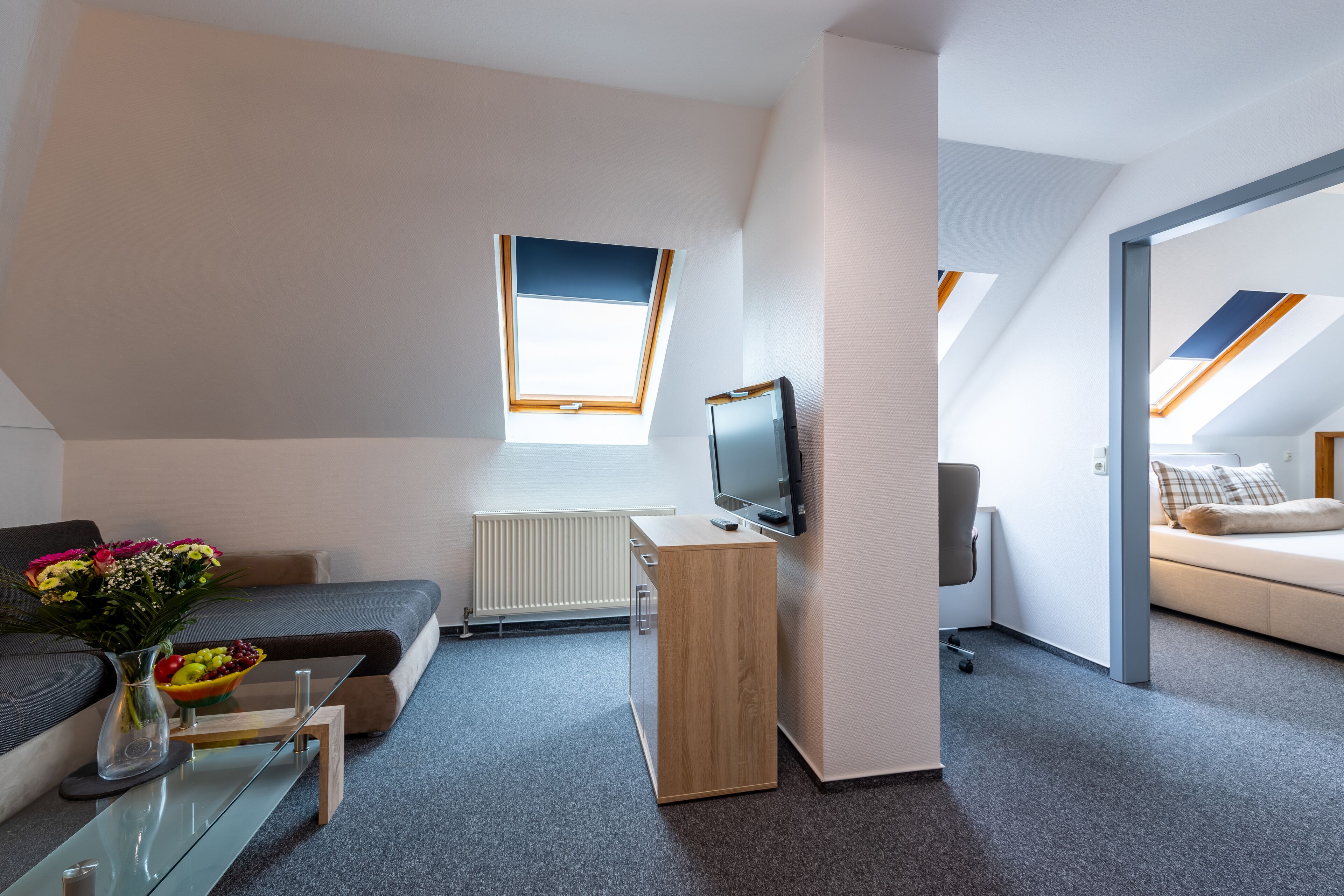 Quarto moderno no estilo loft, com claraboia, cama, escrivaninha e televisão.