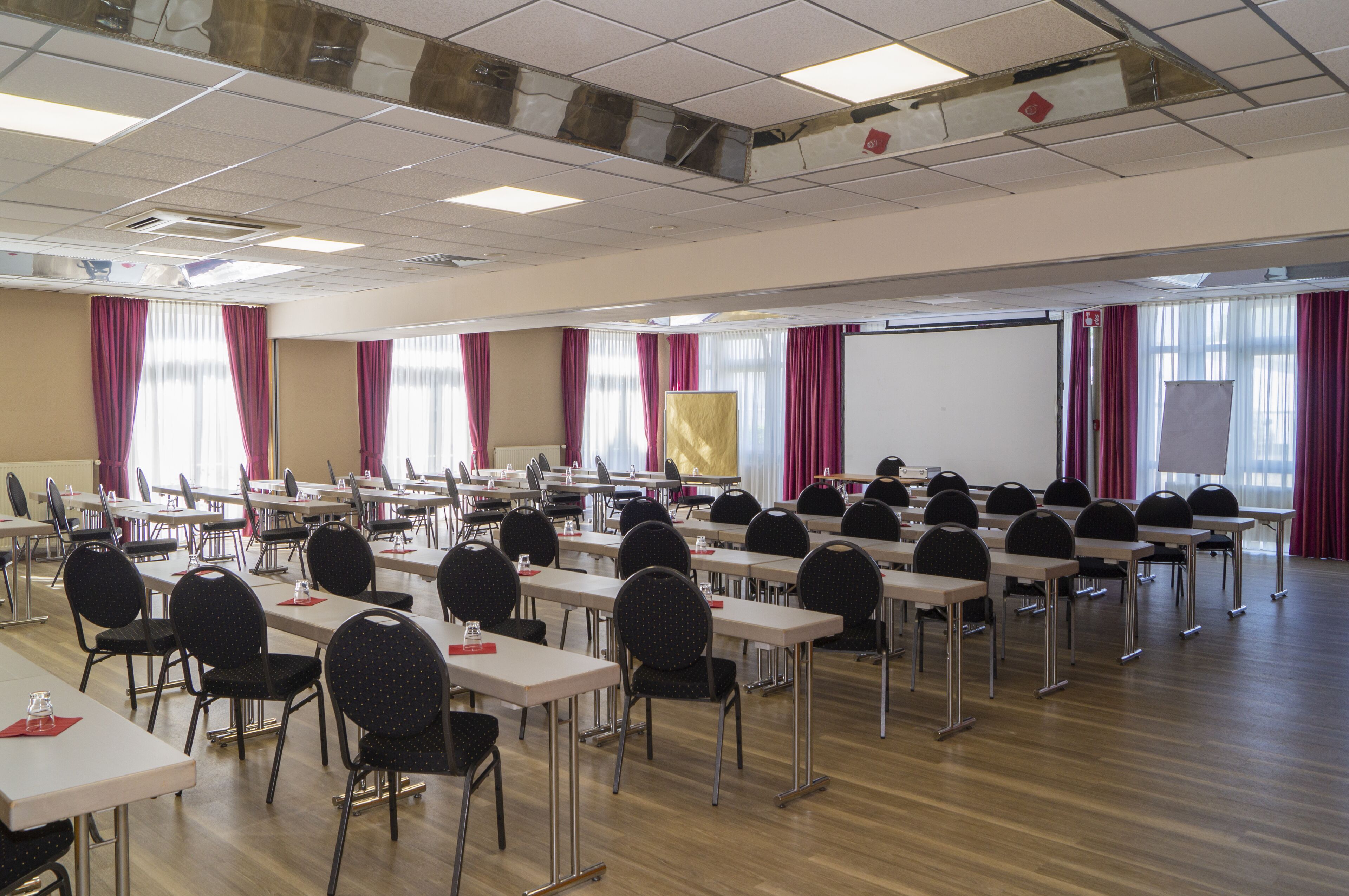 Ein Konferenzraum mit Tischen und Stühlen, einer Projektionsleinwand und Fenstern mit Vorhängen.