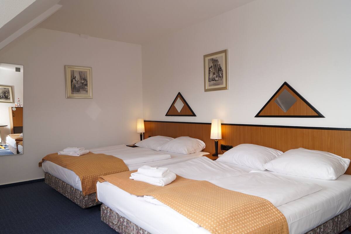 A hotel room with two beds, each with white linens and a brown blanket. There are two wall-mounted lamps on either side of the beds.