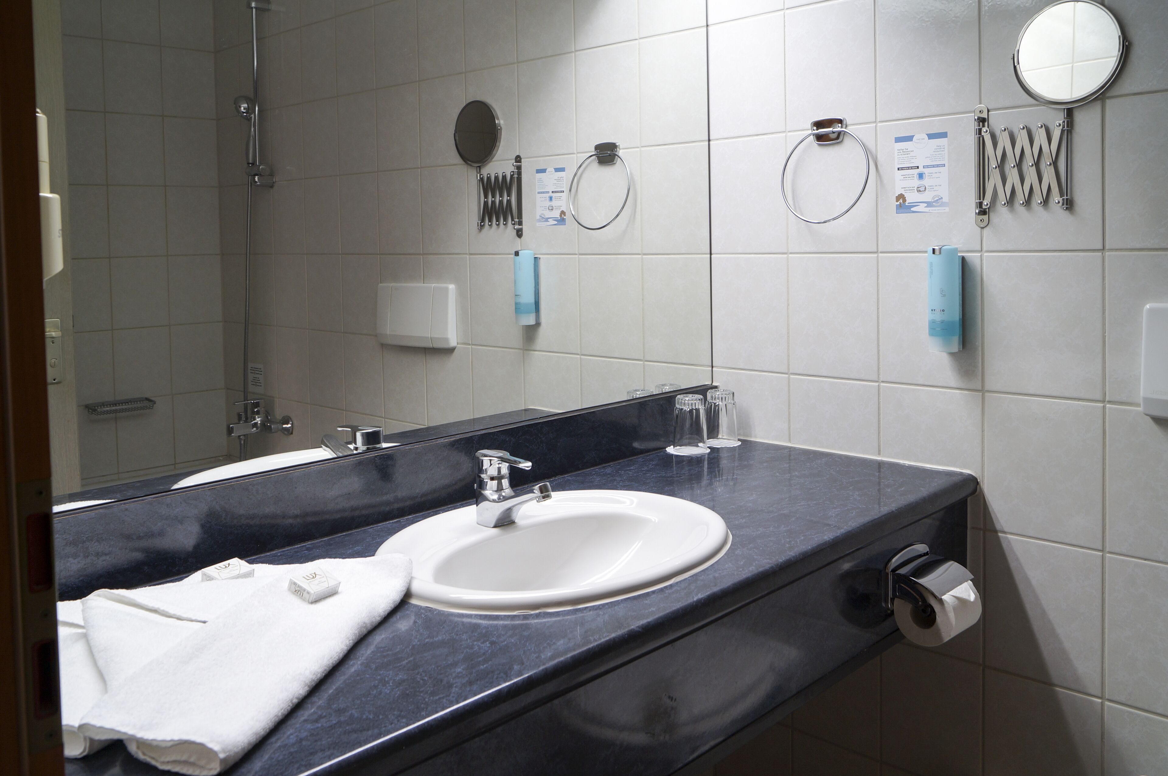 Un baño con lavamanos, espejo, toalla y artículos de aseo.