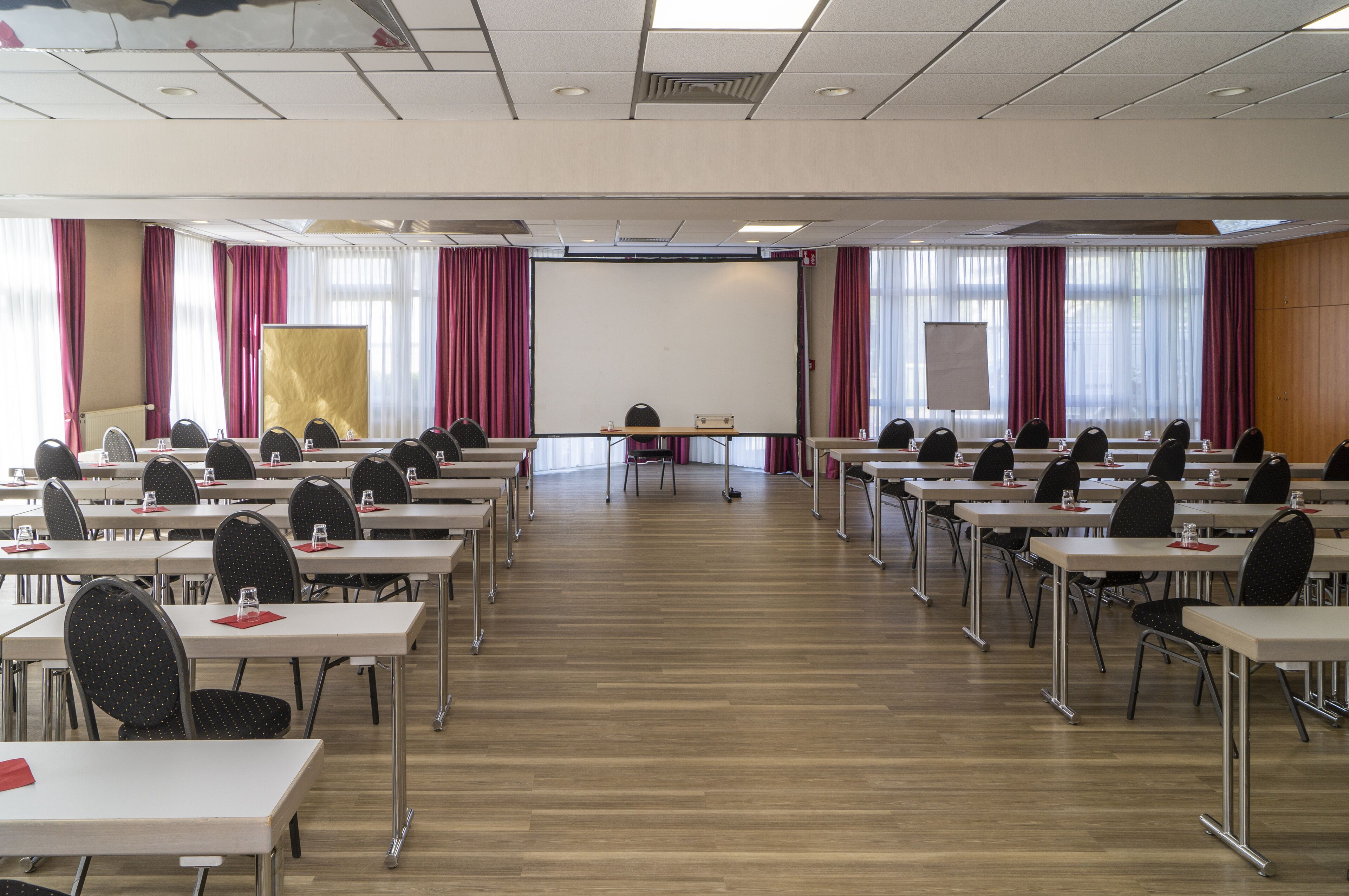Ein Konferenzraum mit Tischen, Stühlen, einer großen Leinwand und einer Whiteboard-Wand.