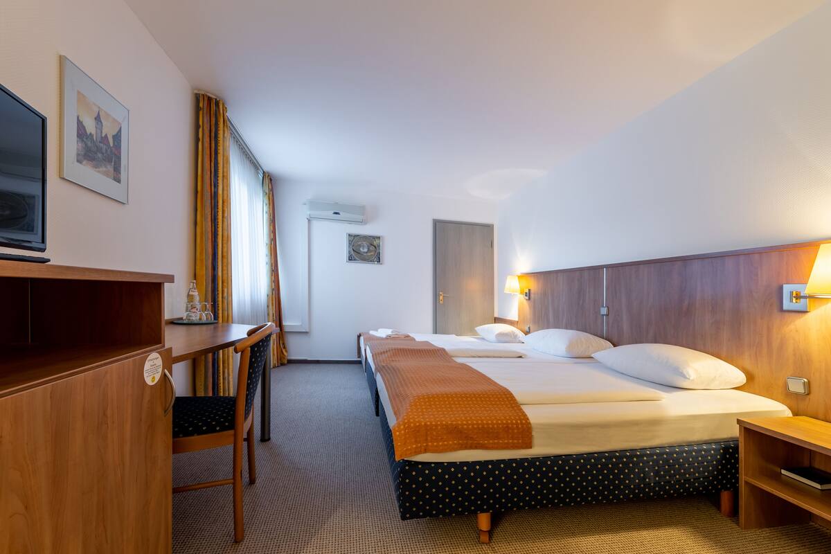A hotel room with a bed, a desk, a chair, a lamp, and a picture on the wall.