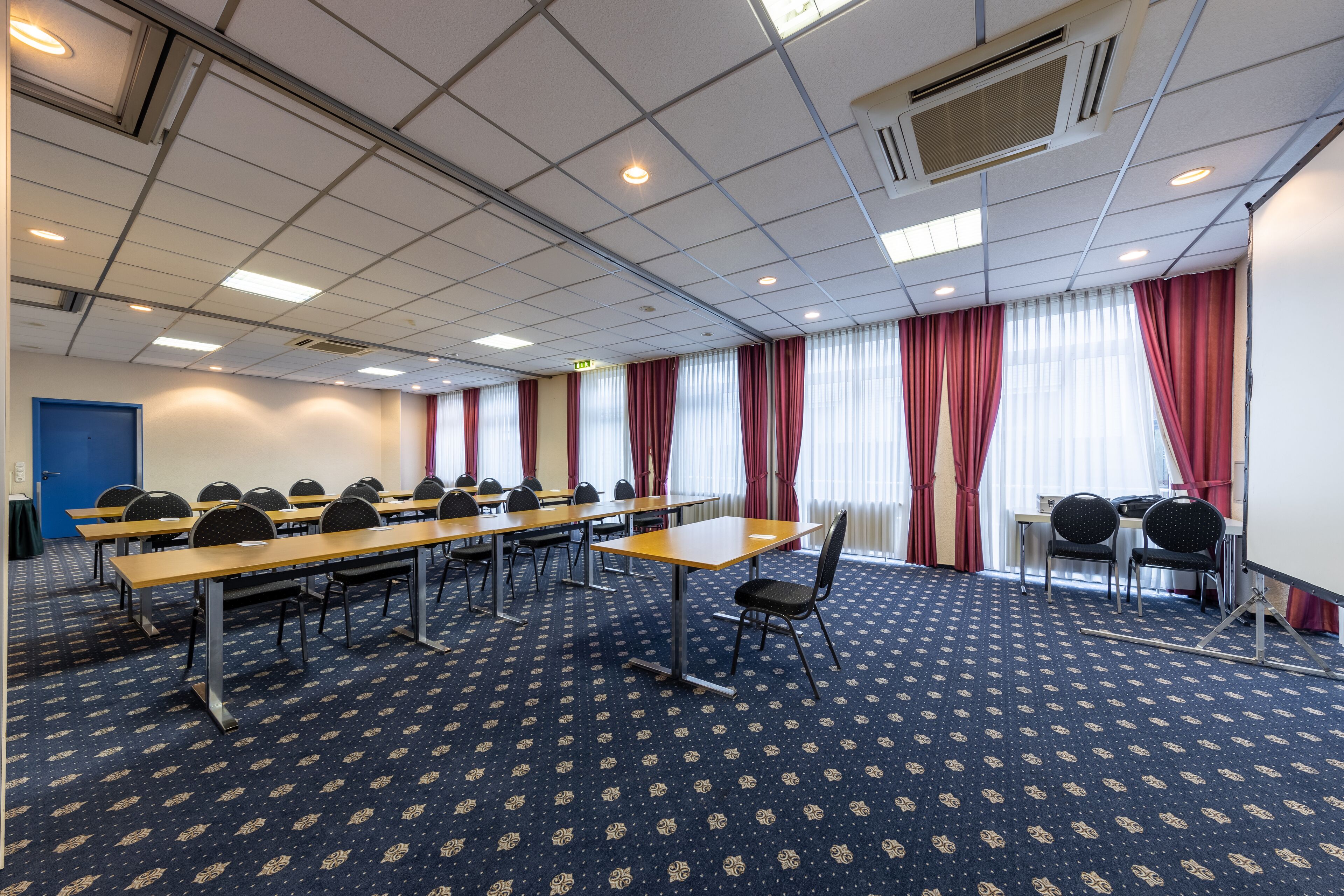 A conference room with multiple tables and chairs, a patterned carpet, and a blue door.