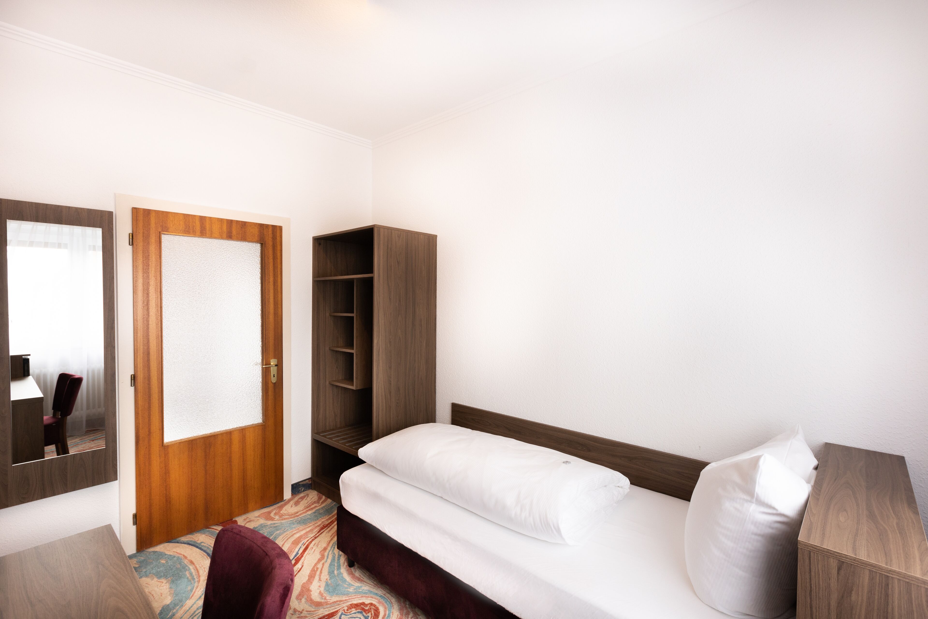 A hotel room with a bed, a wardrobe, a mirror, and a desk.