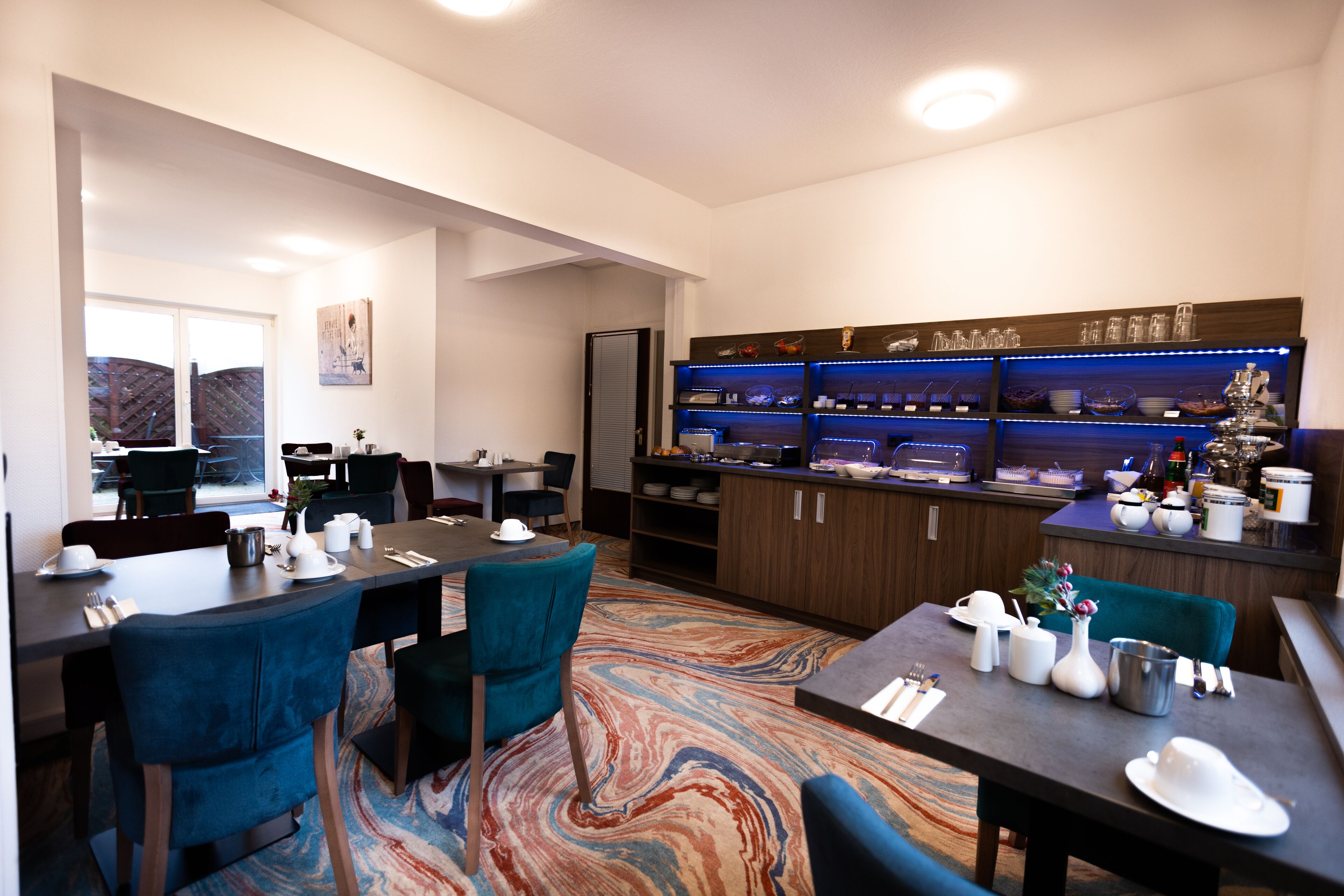A modern dining area with a marble-patterned carpet, a buffet counter with blue lighting, and a view of a fenced outdoor area.