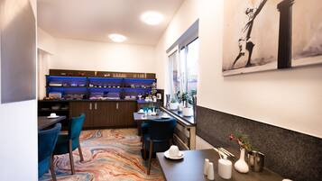 Habitación de hotel con comedor, cocina con iluminación azul, alfombra colorida y un cuadro en la pared.