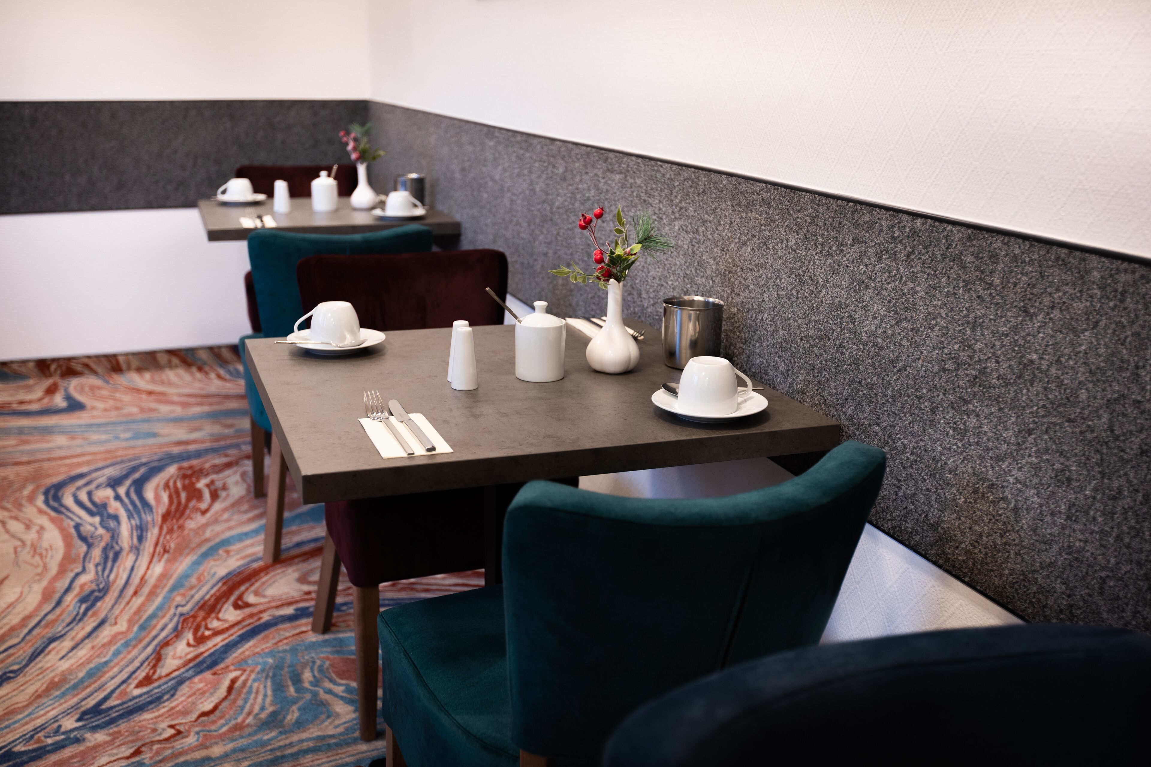 Un comedor con mesas dispuestas para dos, con vajilla blanca y un jarrón con flores.