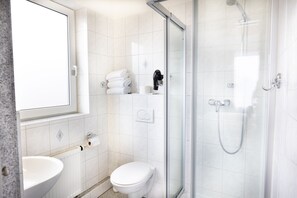 Un baño moderno con ducha de vidrio, inodoro, lavamanos y perchero para toallas.