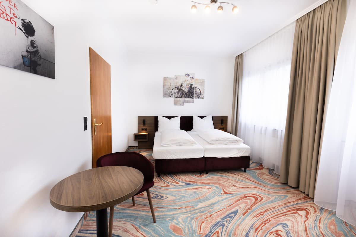 A hotel room with a bed, a chair, a table, and a colorful carpet.