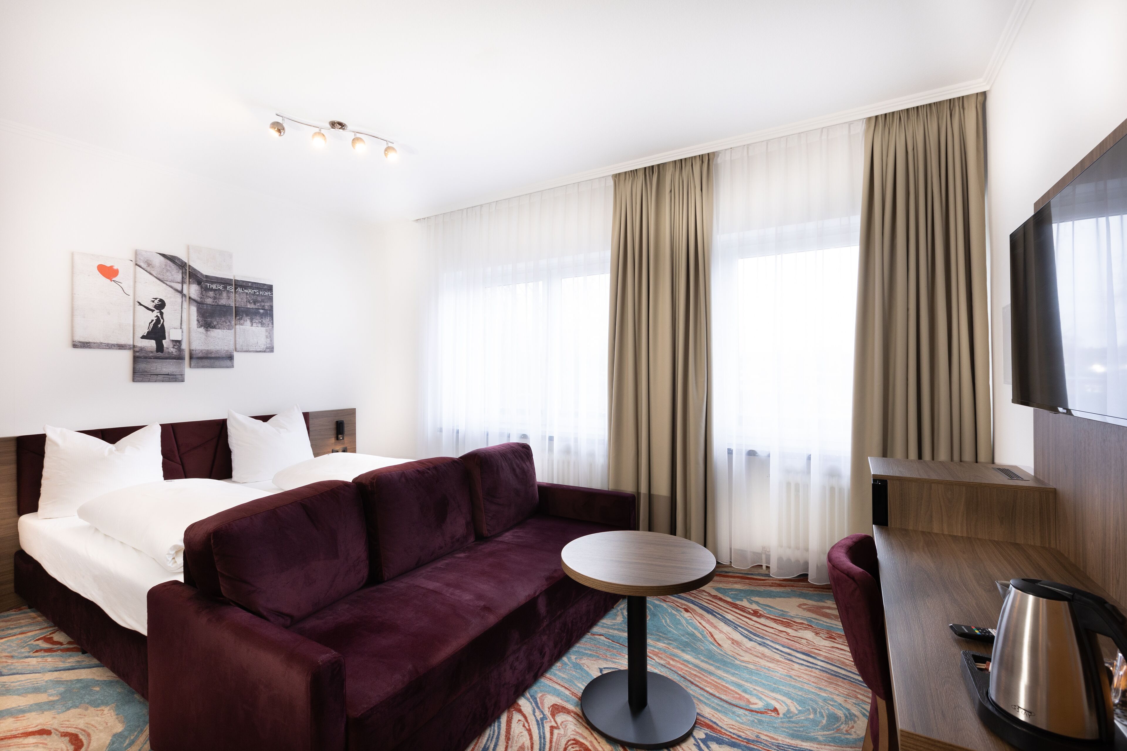 Une chambre d’hôtel avec un grand lit, un canapé, une petite table ronde, une télévision et une fenêtre avec des rideaux.