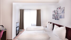 Habitación de hotel con dos camas, un escritorio con cafetera y vistas al exterior a través de ventanas amplias.