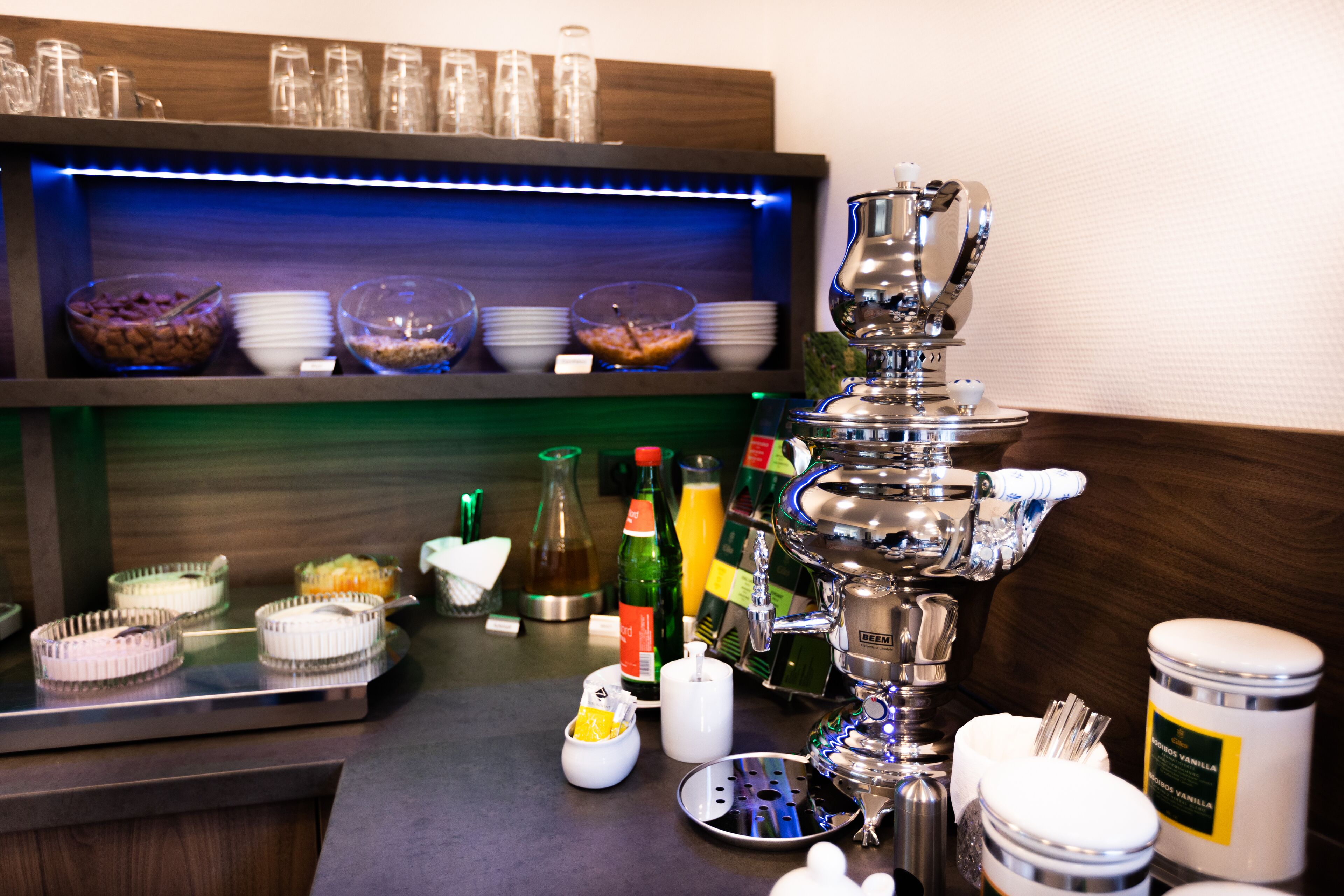 A buffet setup with various food items, condiments, and a beverage dispenser.