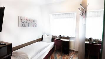 Habitación de hotel con cama, escritorio, silla, radiador y ventana con cortinas.