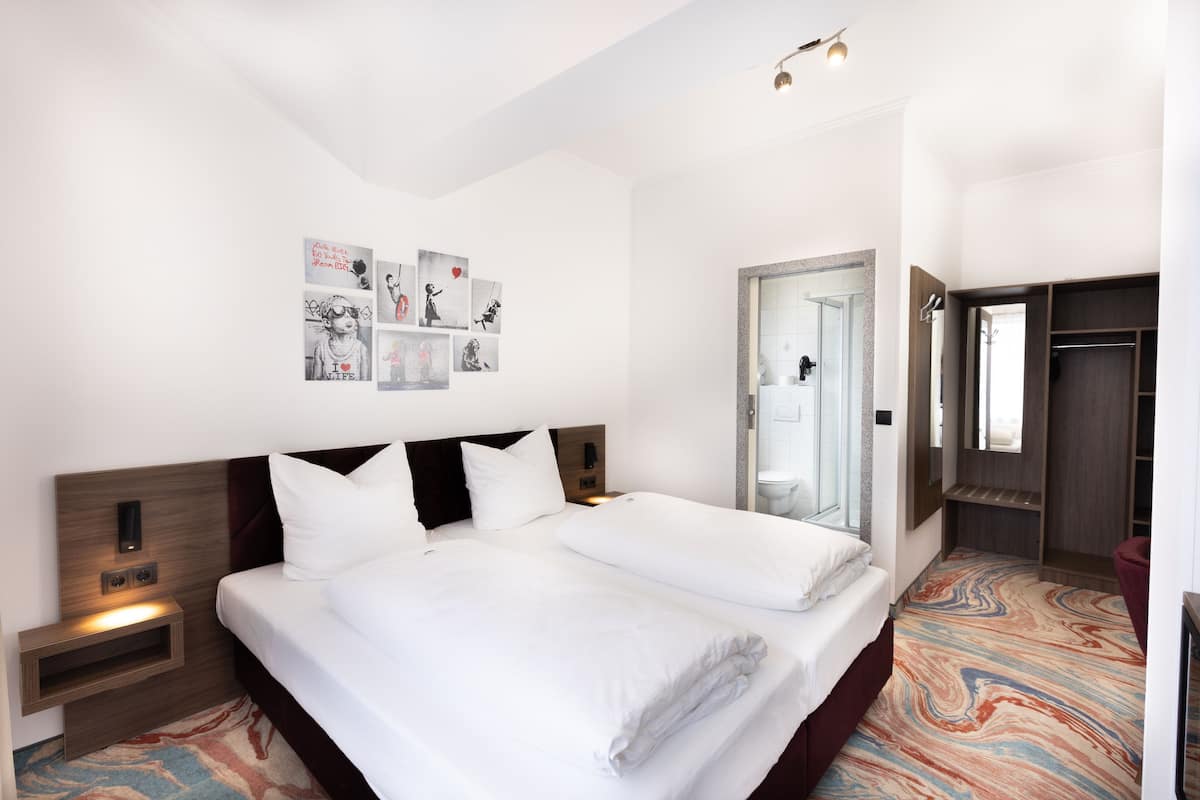 A hotel room with a large bed, a nightstand, a wall-mounted light, a mirror, and a wardrobe.
