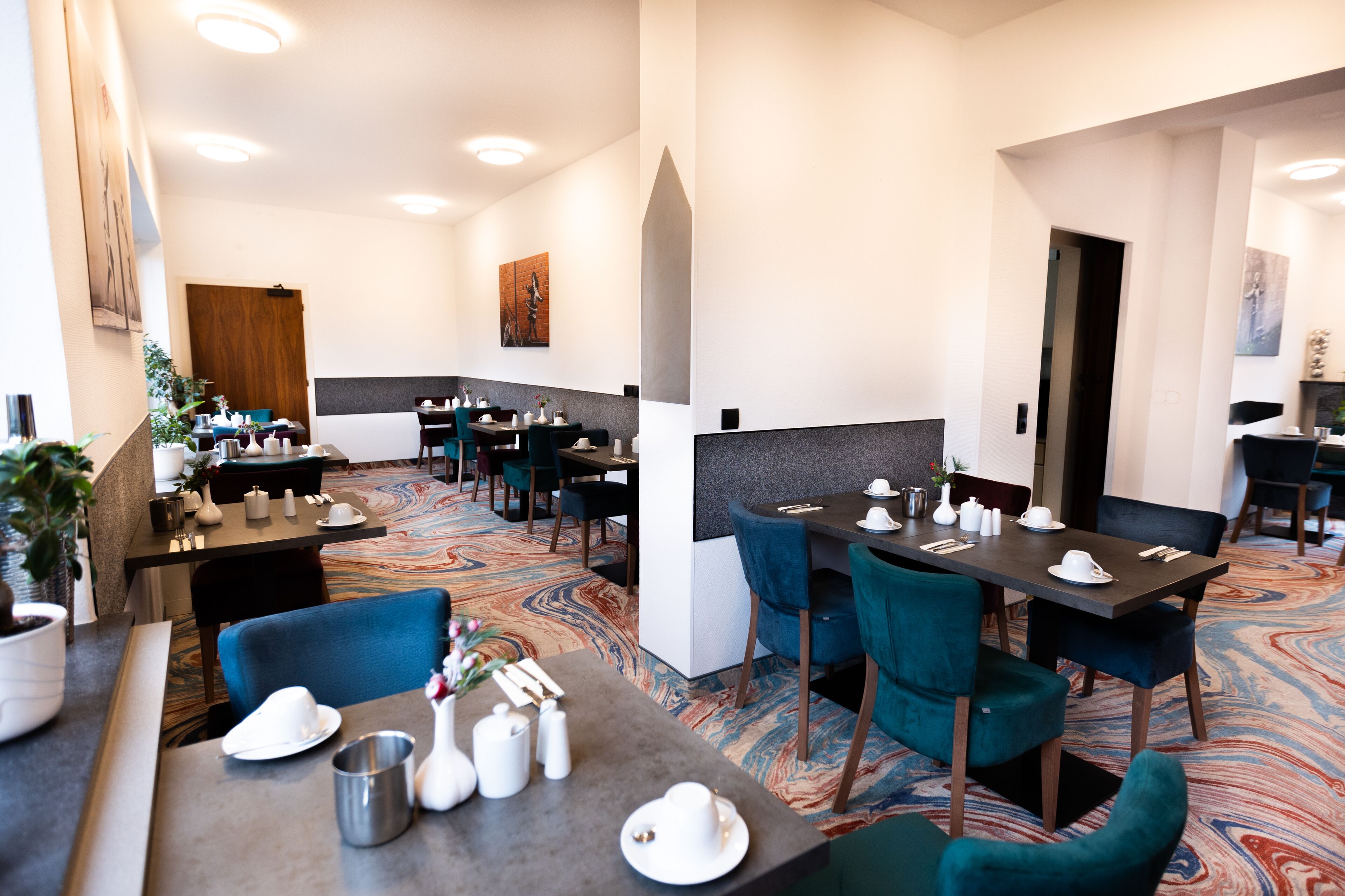 A hotel dining area with multiple tables and chairs, a patterned carpet, and a modern interior design.