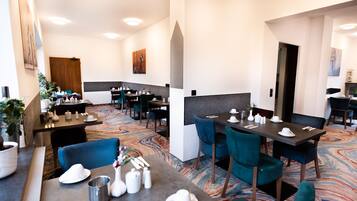 Ein Hotel-Essbereich mit mehreren Tischen und Stühlen, einem gemusterten Teppich und einem modernen Interieur.