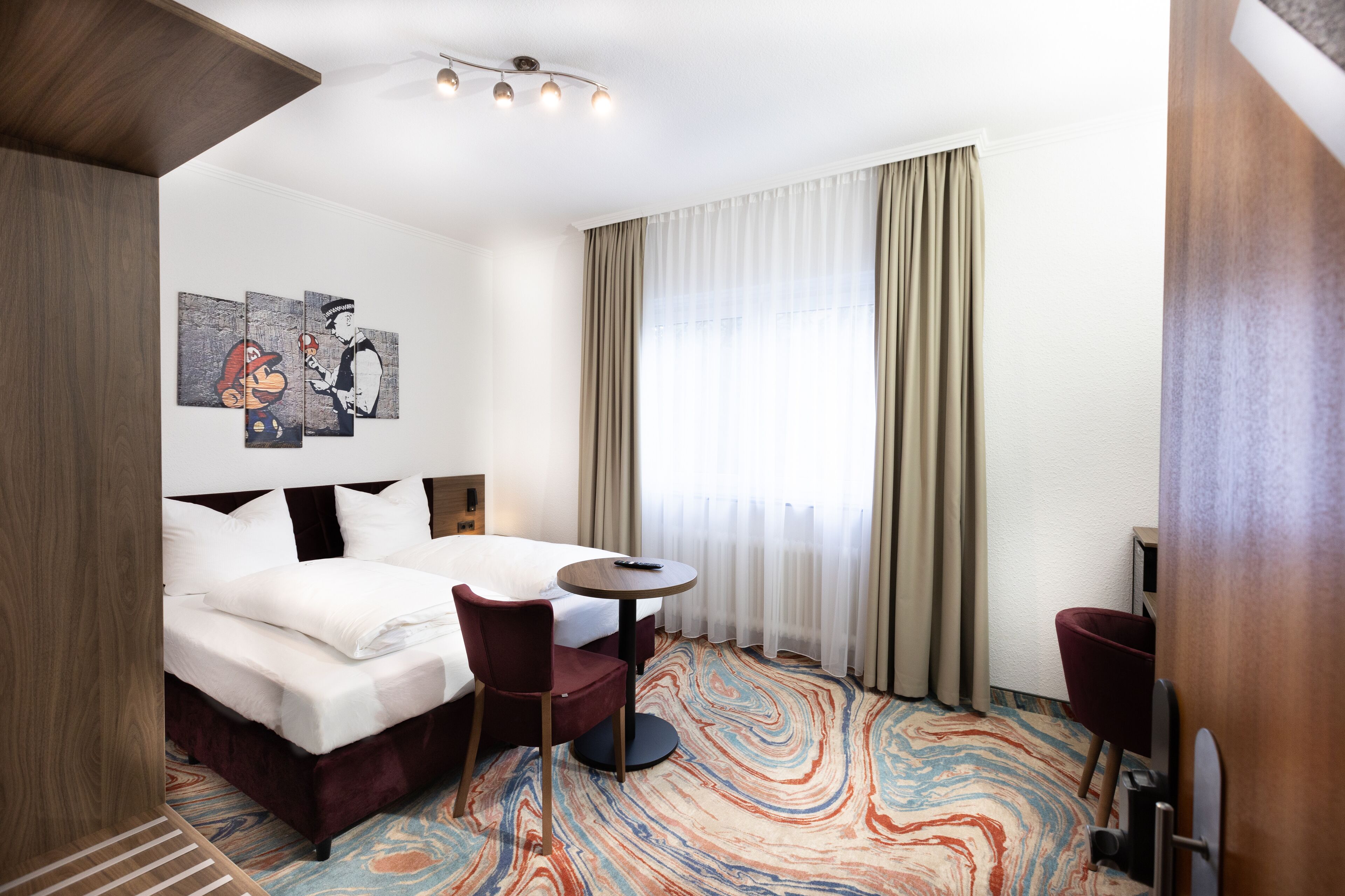 Habitación de hotel con una cama, dos sillas, una mesita y un cuadro en la pared.