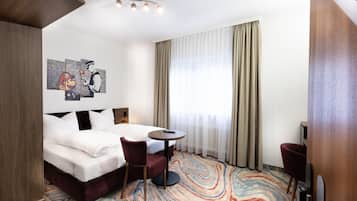 Habitación de hotel con una cama, dos sillas, una mesita y un cuadro en la pared.