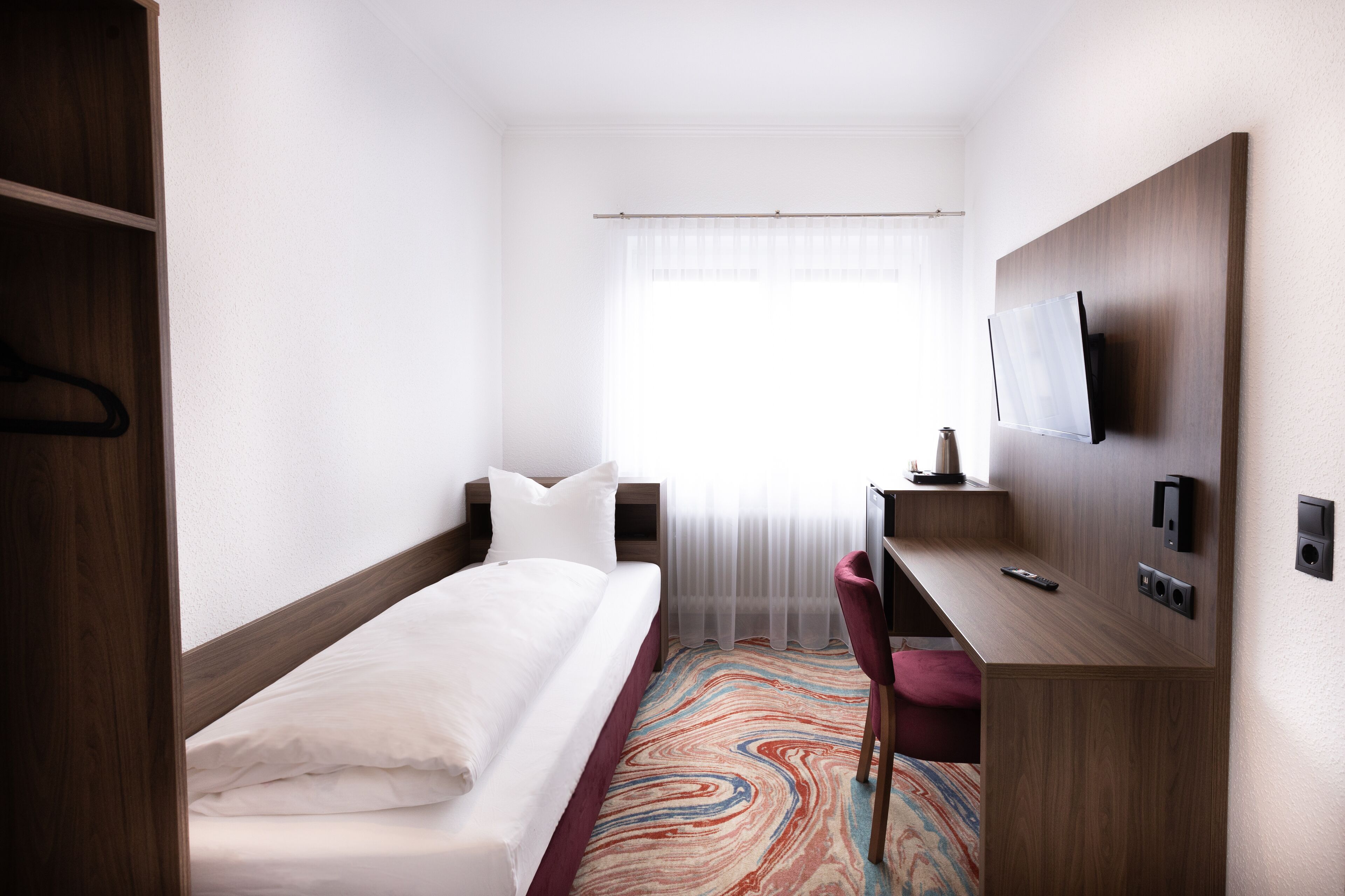 A hotel room with a bed, a desk, a chair, a TV, and a window with curtains.