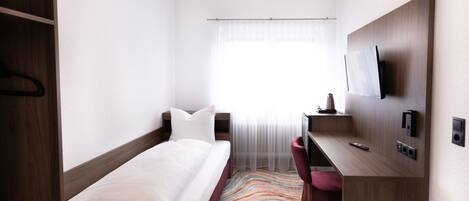 A hotel room with a bed, a desk, a chair, a TV, and a window with curtains.
