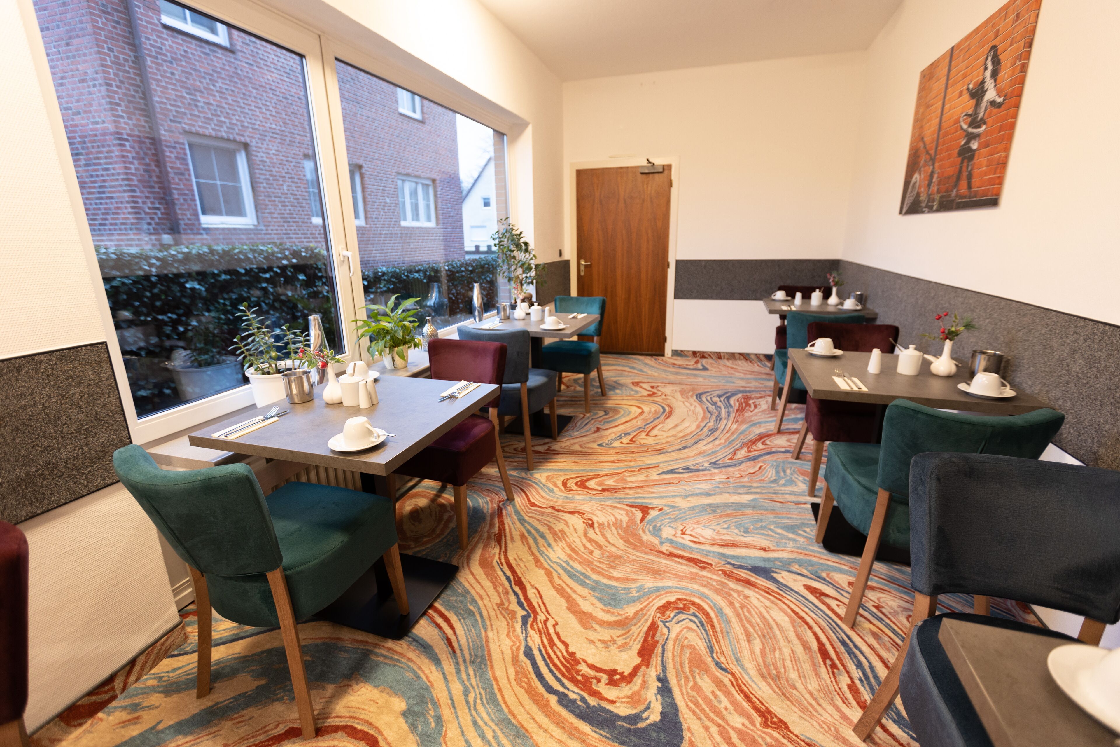 A dining area with tables and chairs, a patterned carpet, and a view of a brick building outside.