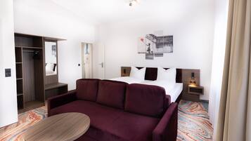 Ein Hotelzimmer mit einem Bett, einem Sofa, einem kleinen Tisch, einem Schrank und einem an der Wand hängenden Kunstwerk.