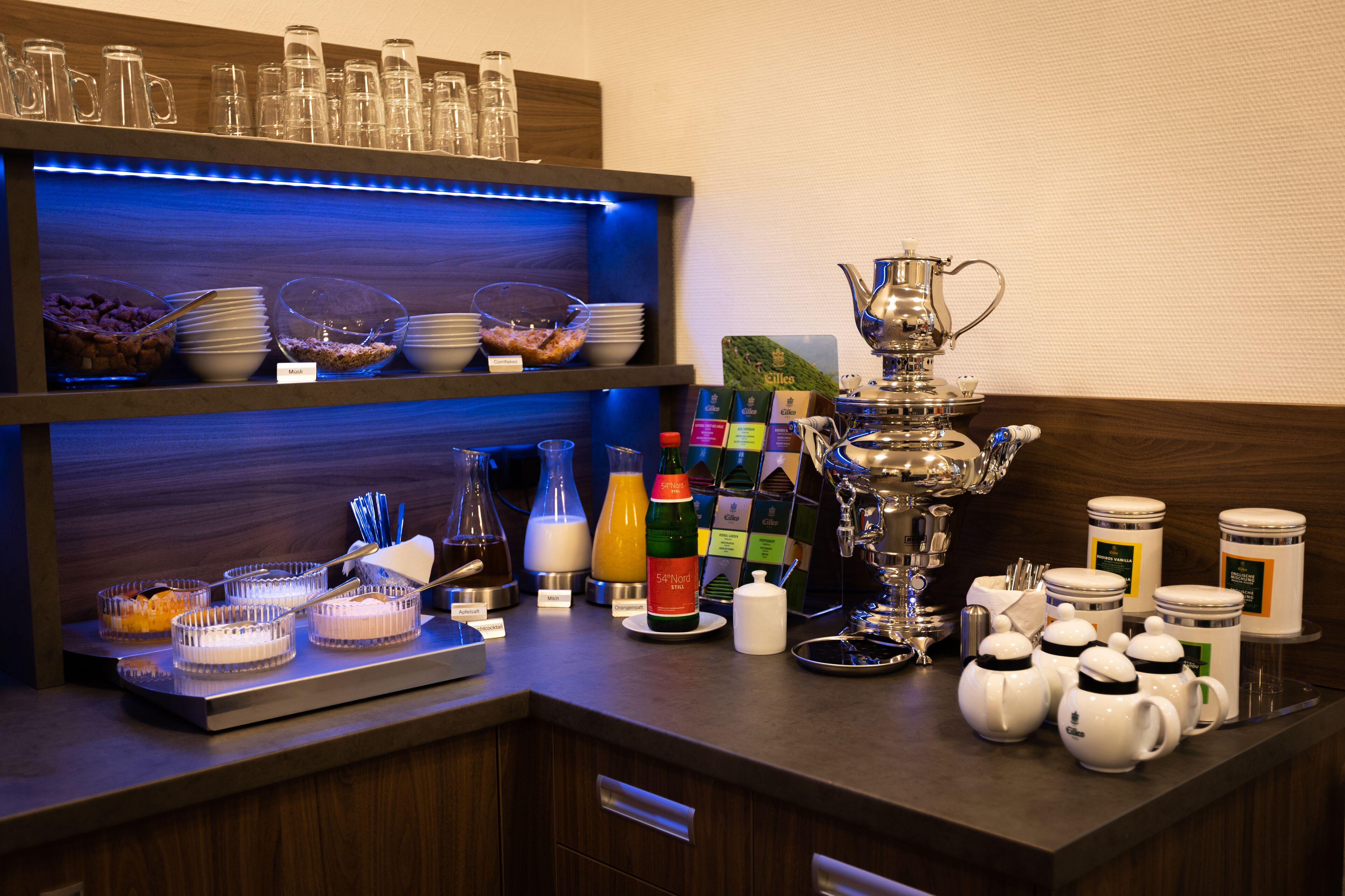 A buffet setup with various food items, beverages, and utensils.