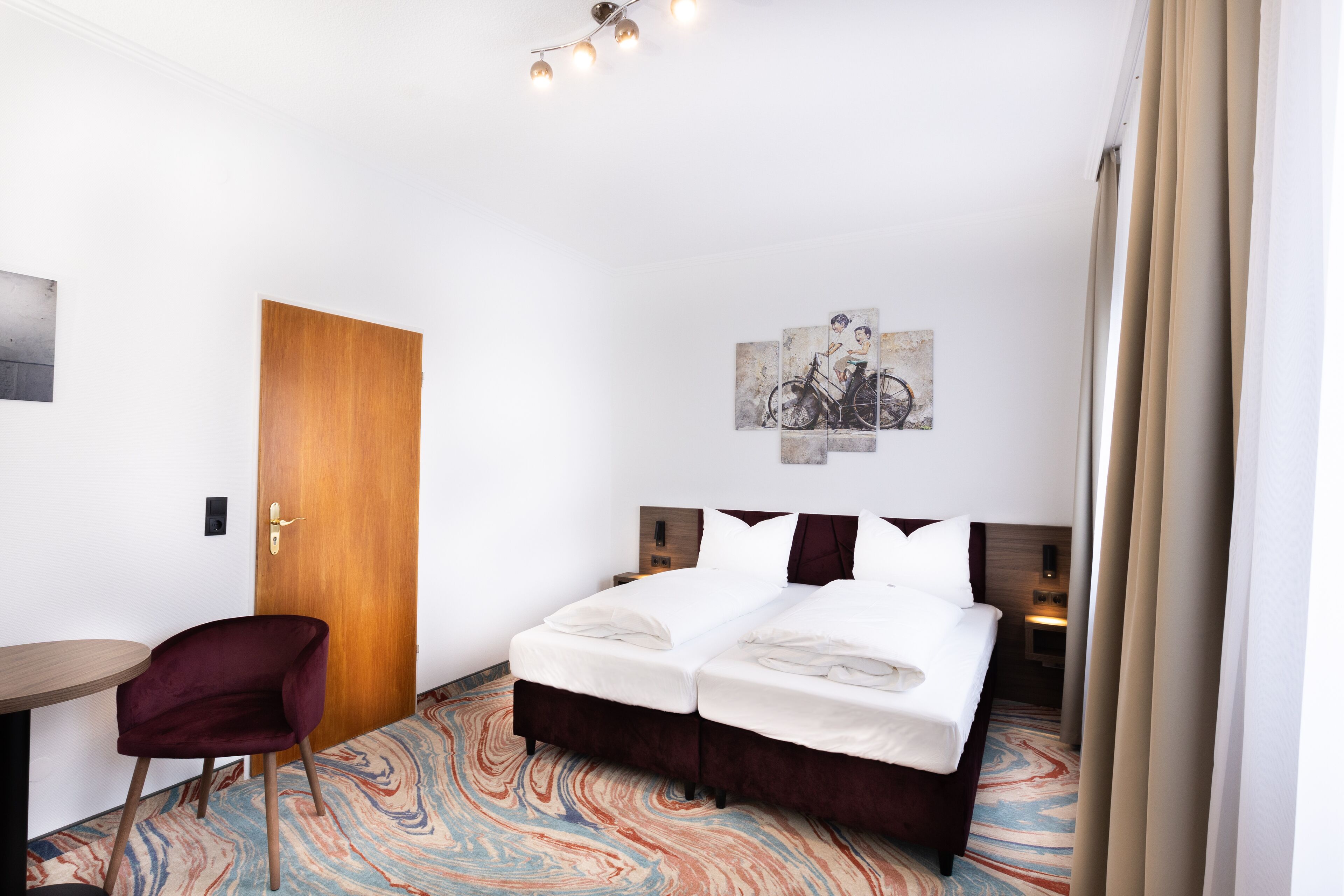 Ein Hotelzimmer mit einem Bett, einem Sessel, einem Schreibtisch und einem Wandbild.
