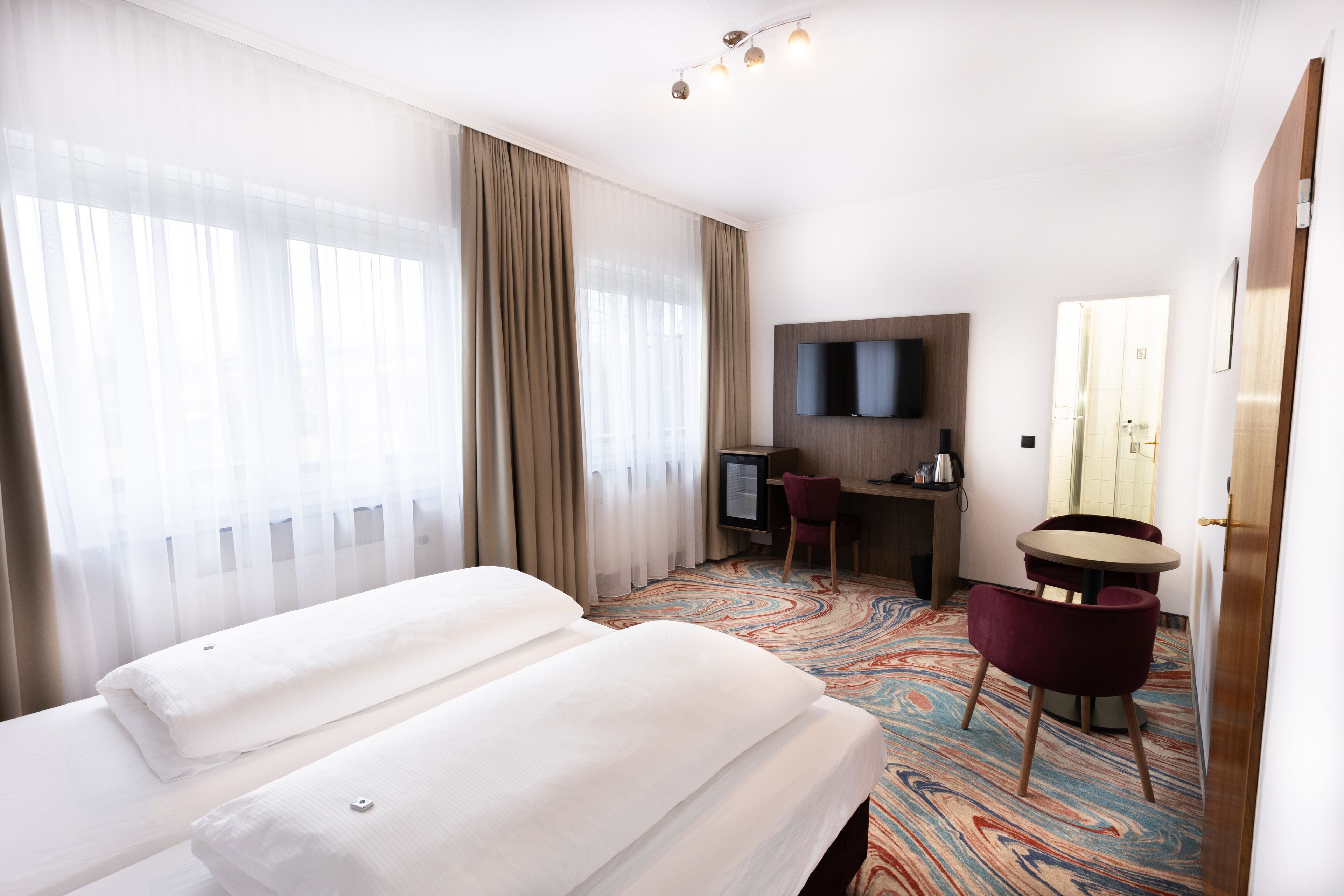 A hotel room with two beds, a desk with a chair, a television, and a patterned carpet.
