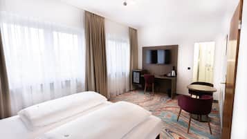 A hotel room with two beds, a desk with a chair, a television, and a patterned carpet.