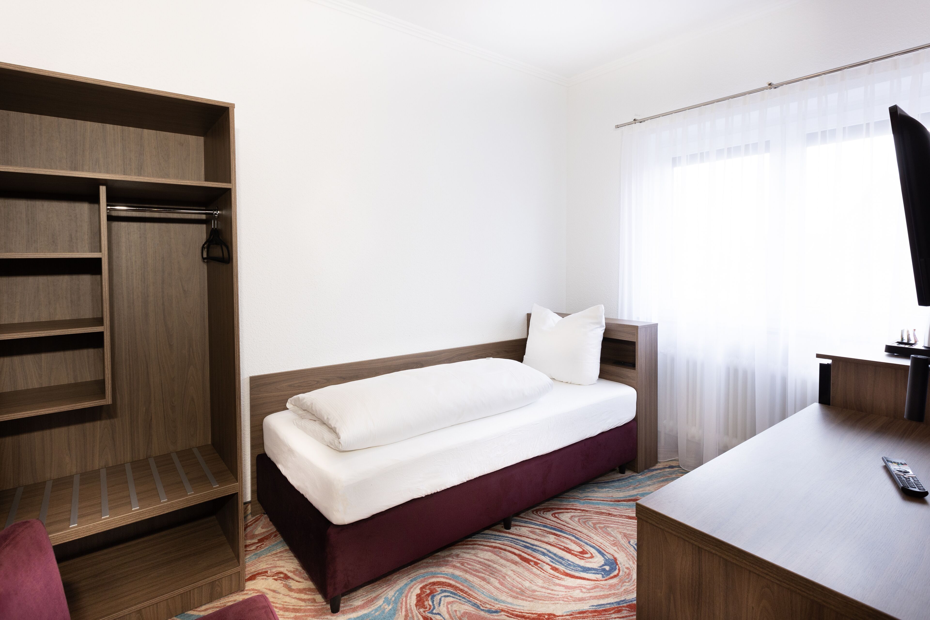 A hotel room with a bed, a desk, a wardrobe, and a television.