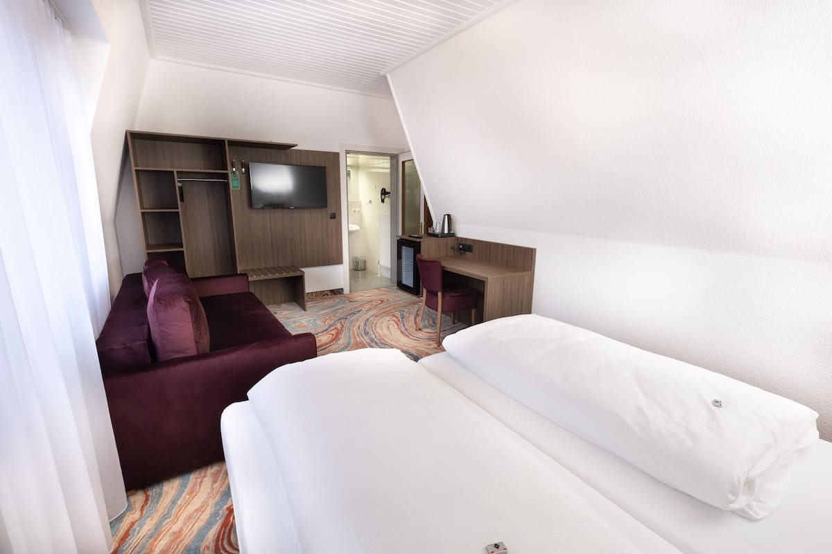 A hotel room with a bed, a sofa, a desk, a TV, and a wardrobe.