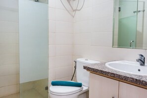 A bathroom with a white toilet, a sink with a granite countertop, and a mirror above the sink. - City View 1BR Apartment at Woodland Park Residence (Jakarta)