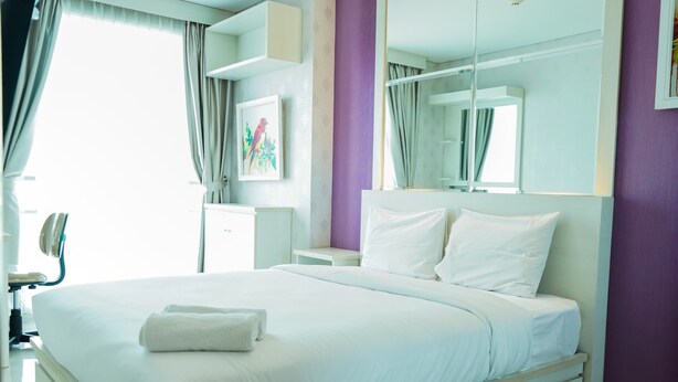 A modern hotel room with a large bed, a bedside table, a mirror, and a window with curtains. - City View 1BR Apartment at Woodland Park Residence (Jakarta)