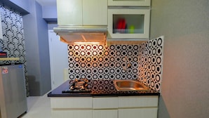 A compact kitchen with a patterned backsplash, a stainless steel sink, and a built-in microwave. - Furnished Studio Green Pramuka City Apartment (Jakarta)