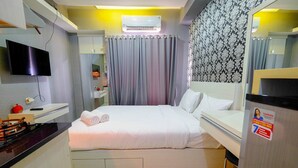 A hotel room with a bed, a TV, an air conditioner, a mirror, and a refrigerator. - Furnished Studio Green Pramuka City Apartment (Jakarta)