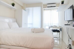 A hotel room with a large bed, a desk with a chair, a TV mounted on the wall, and a window with curtains.