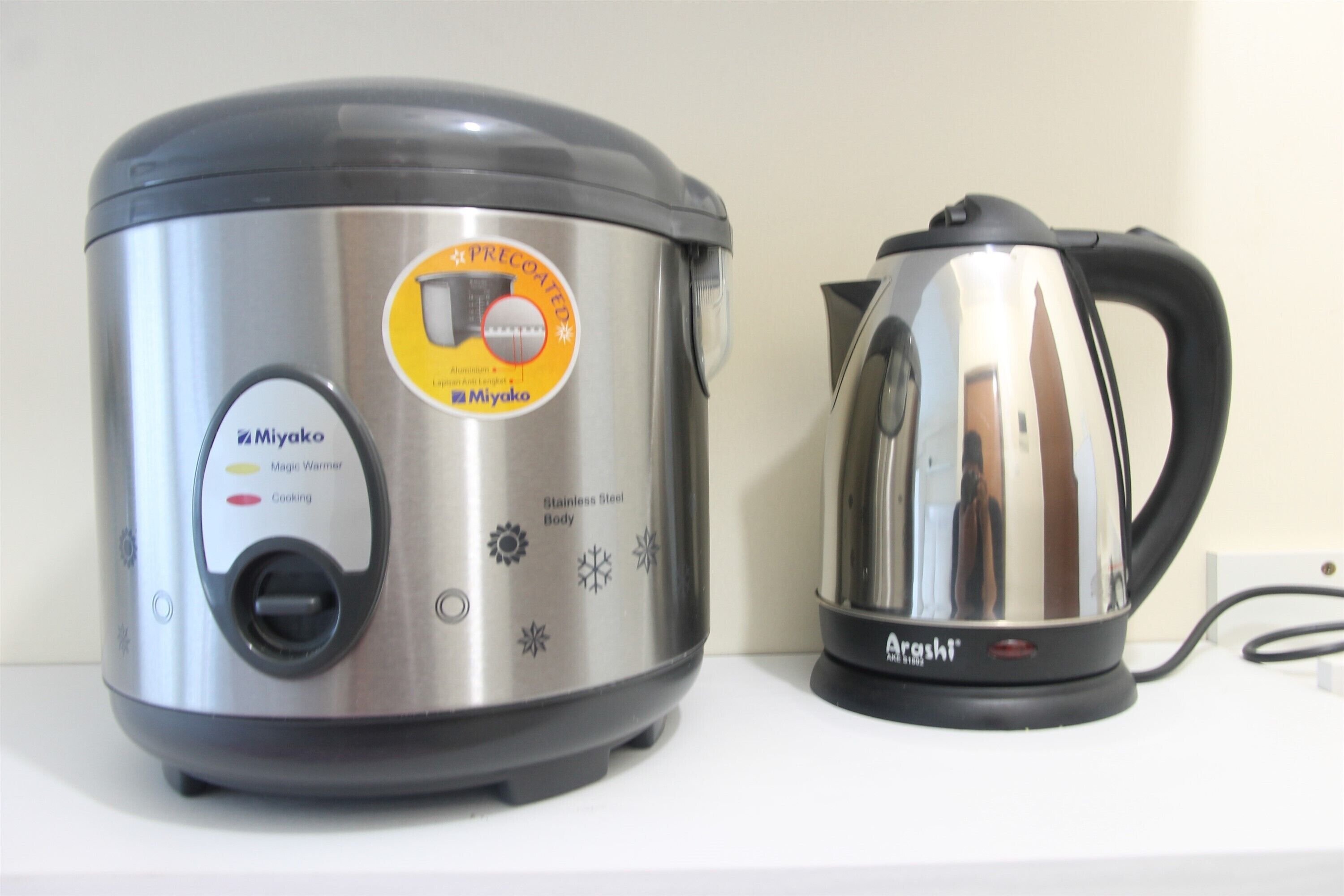 A stainless steel electric pressure cooker and a kettle on a white countertop.
